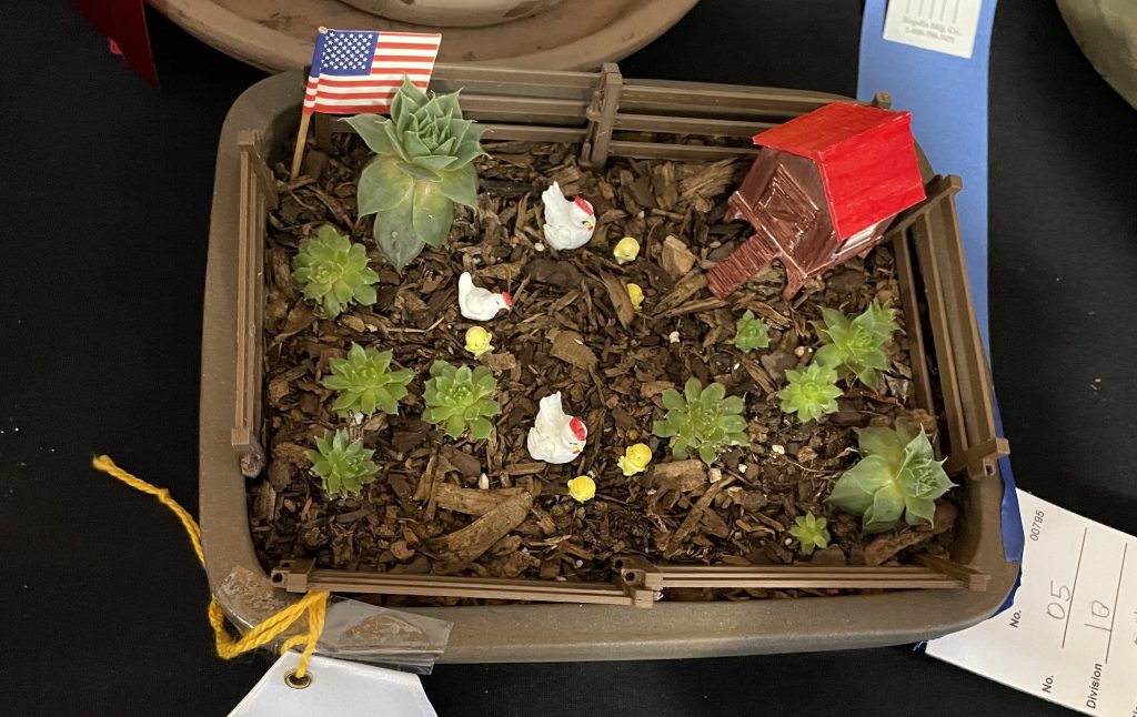 Hens and chicks succulents planted with hens and chicks figurines and a tiny brown chicken coop with a red top.